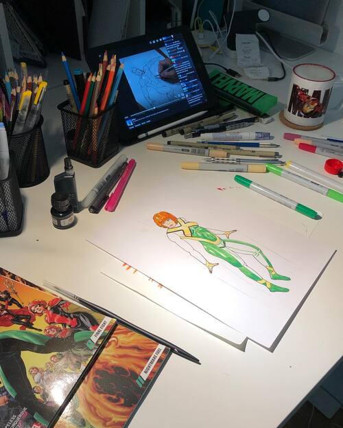 pic of my desk while drawing with a lot of copic markers and an iPad with a Jim Lee twich stream in the background from a different angle